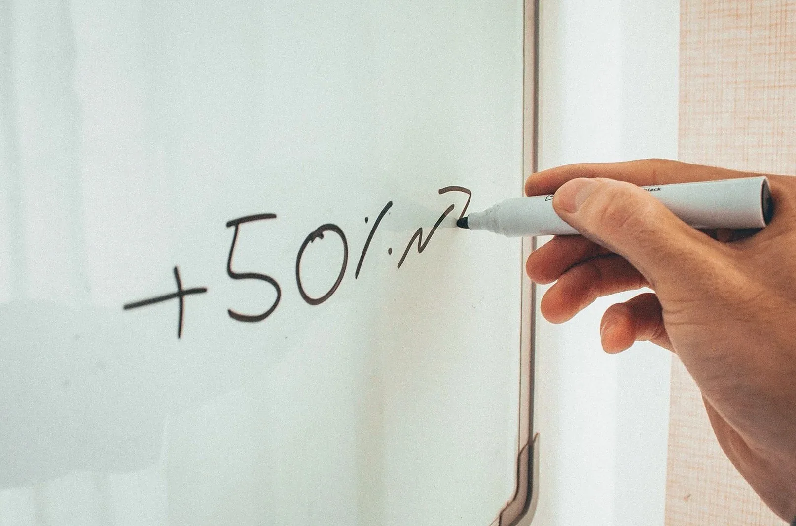 ホワイトボードに「+50%」と書き込む手元